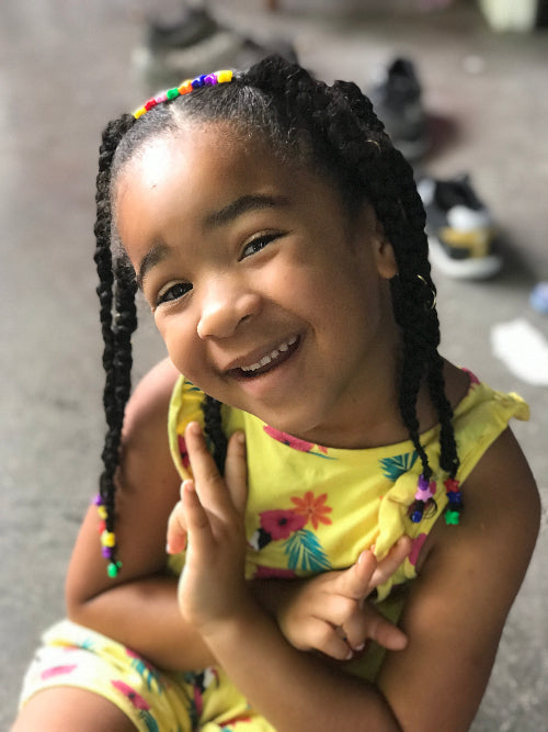 Petite fille souriante avec une coiffure twistée, perles colorées et accessoires sur cheveux afro.