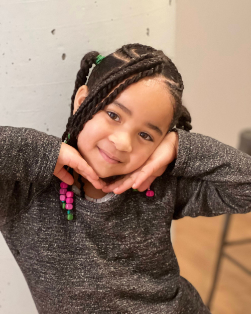 Enfant souriante avec coiffure tressée en cœur et accessoires roses et verts