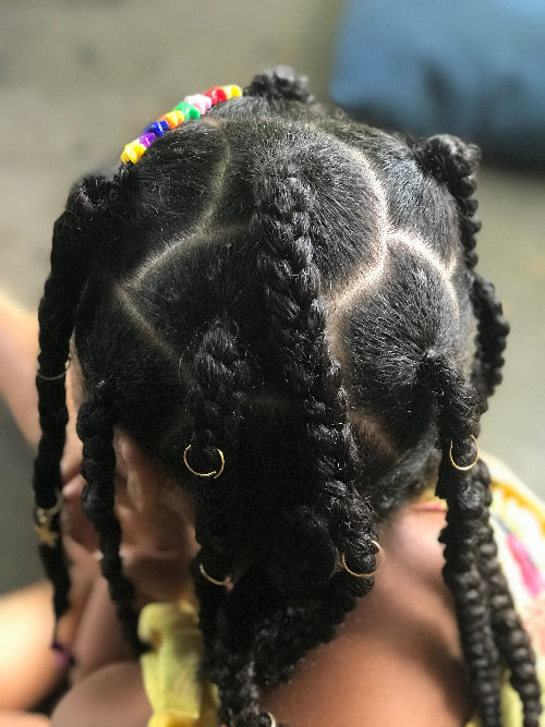 Vue de côté d'une coiffure protectrice twistée avec séparations nettes et accessoires dorés (bagues) sur cheveux afro.