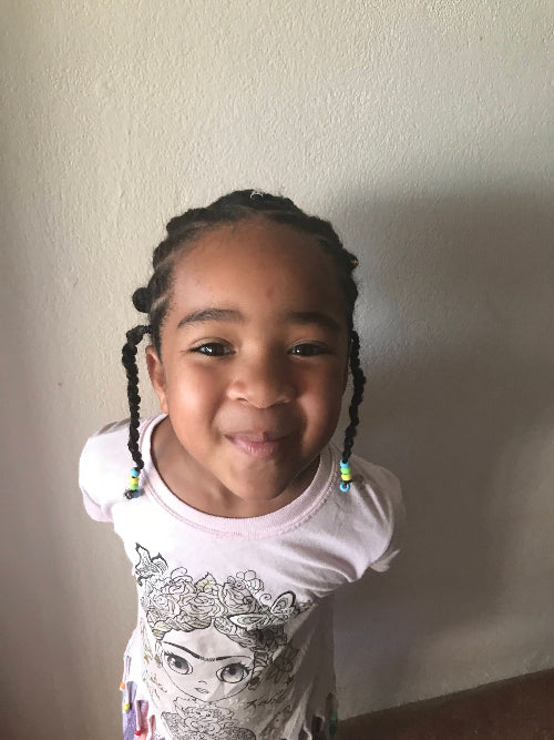 Fille souriante coiffée avec des twists et des perles jaunes, vertes et bleues en bout de tresse, dans un tutoriel coiffure.
