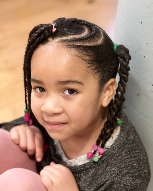 Petite fille avec une coiffure twist en forme de cœur et perles colorées, vue de face