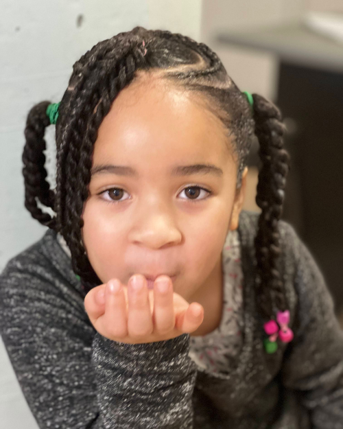 Petite fille coiffée de twists faisant un bisou vers la caméra, coiffure avec perles colorées