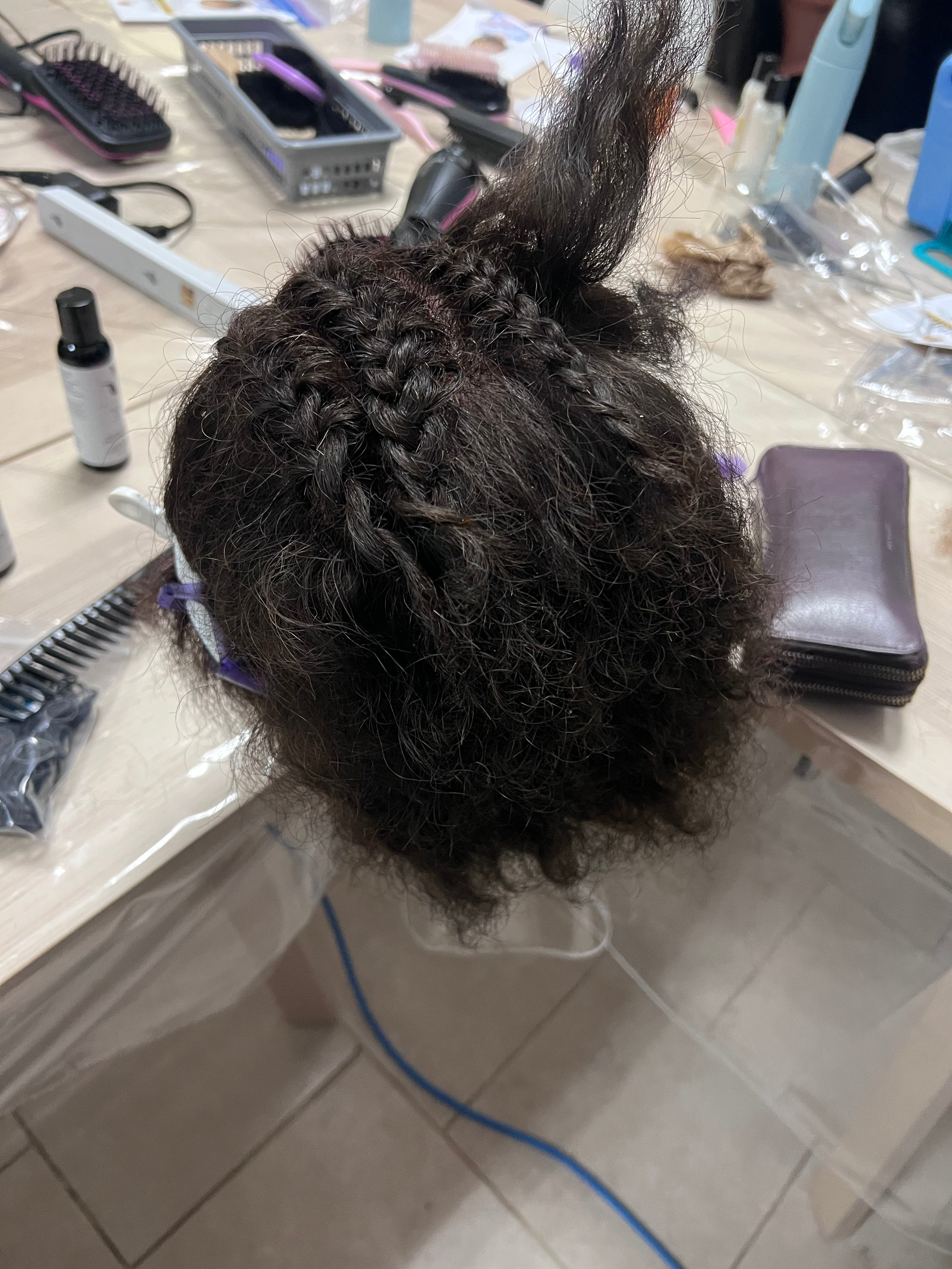 Vue de dessus d’une tête à coiffer avec des tresses en cours de réalisation et des sections maintenues par des pinces.
