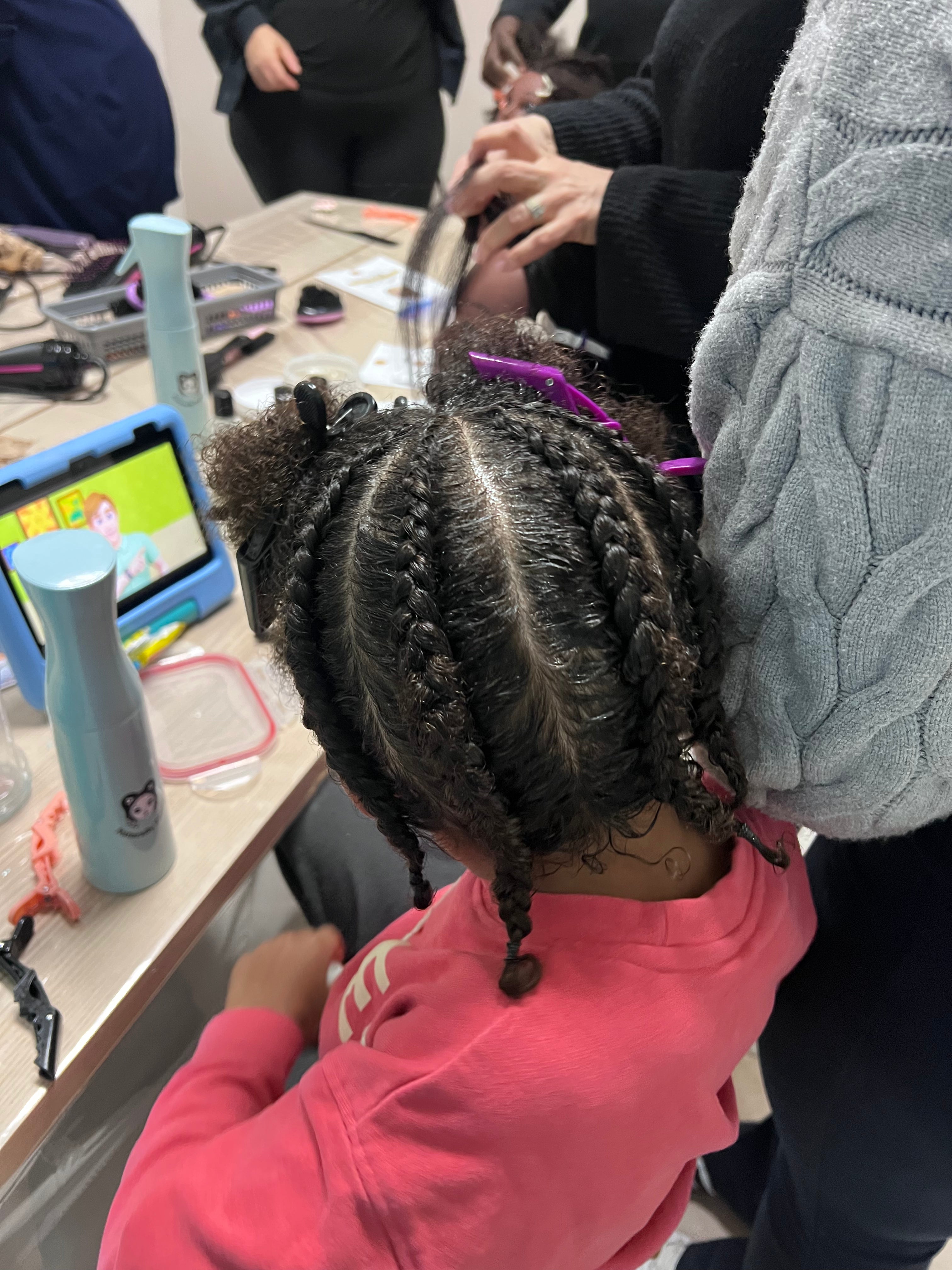 Vue de dessus des tresses collées d’un enfant pendant la mise en pratique, avec les sections restantes retenues par des pinces.