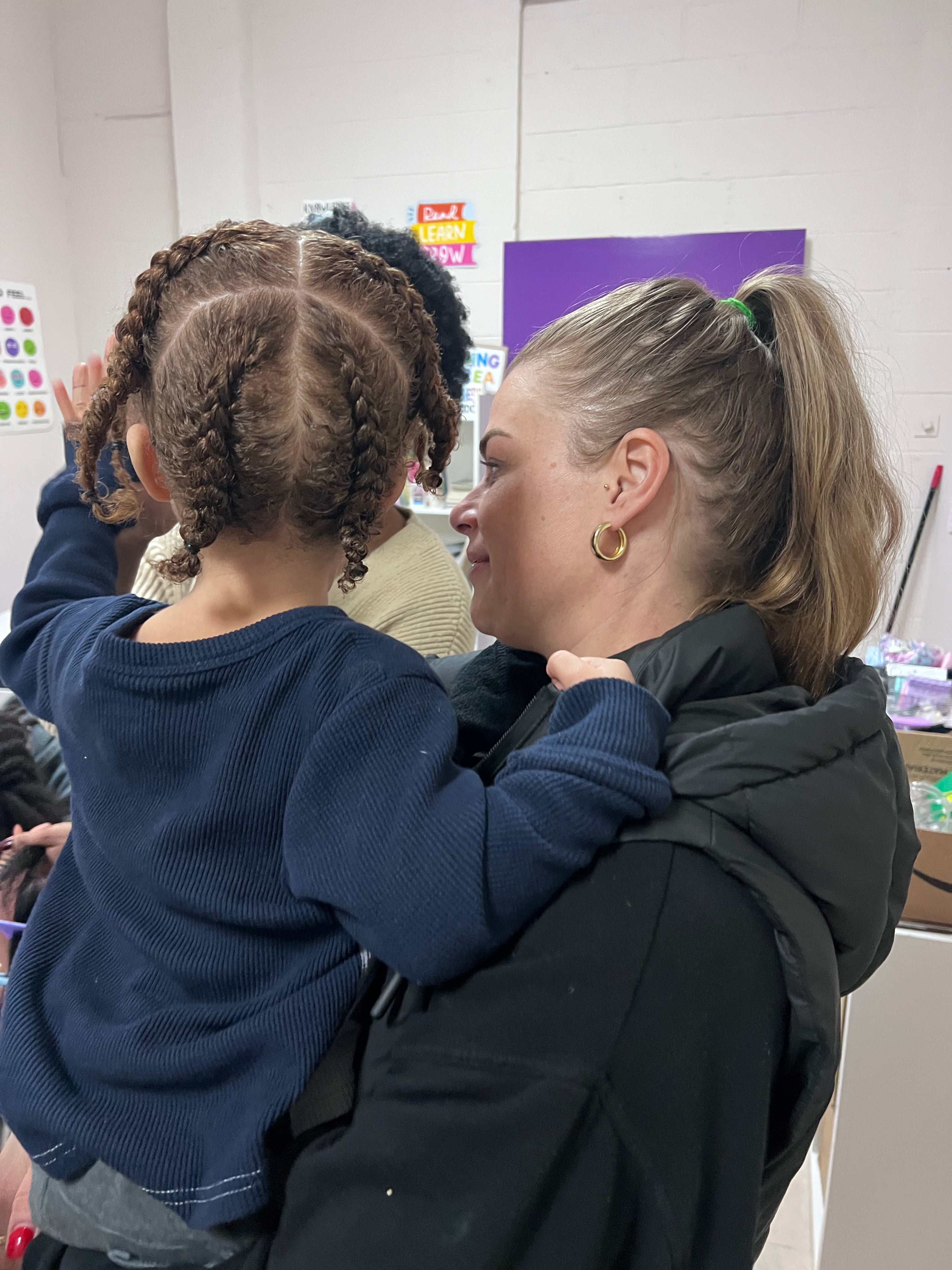Vue arrière des tresses collées d’un enfant, avec des séparations géométriques, dans les bras d’une adulte.