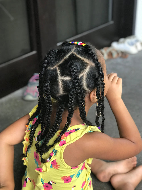 Coiffure enfant avec twists sur cheveux texturés, séparations nettes en triangle et accessoires dorés.