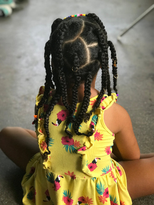 Vue de dos d'une coiffure twistée sur petite fille, avec élastiques, anneaux dorés et perles colorées.