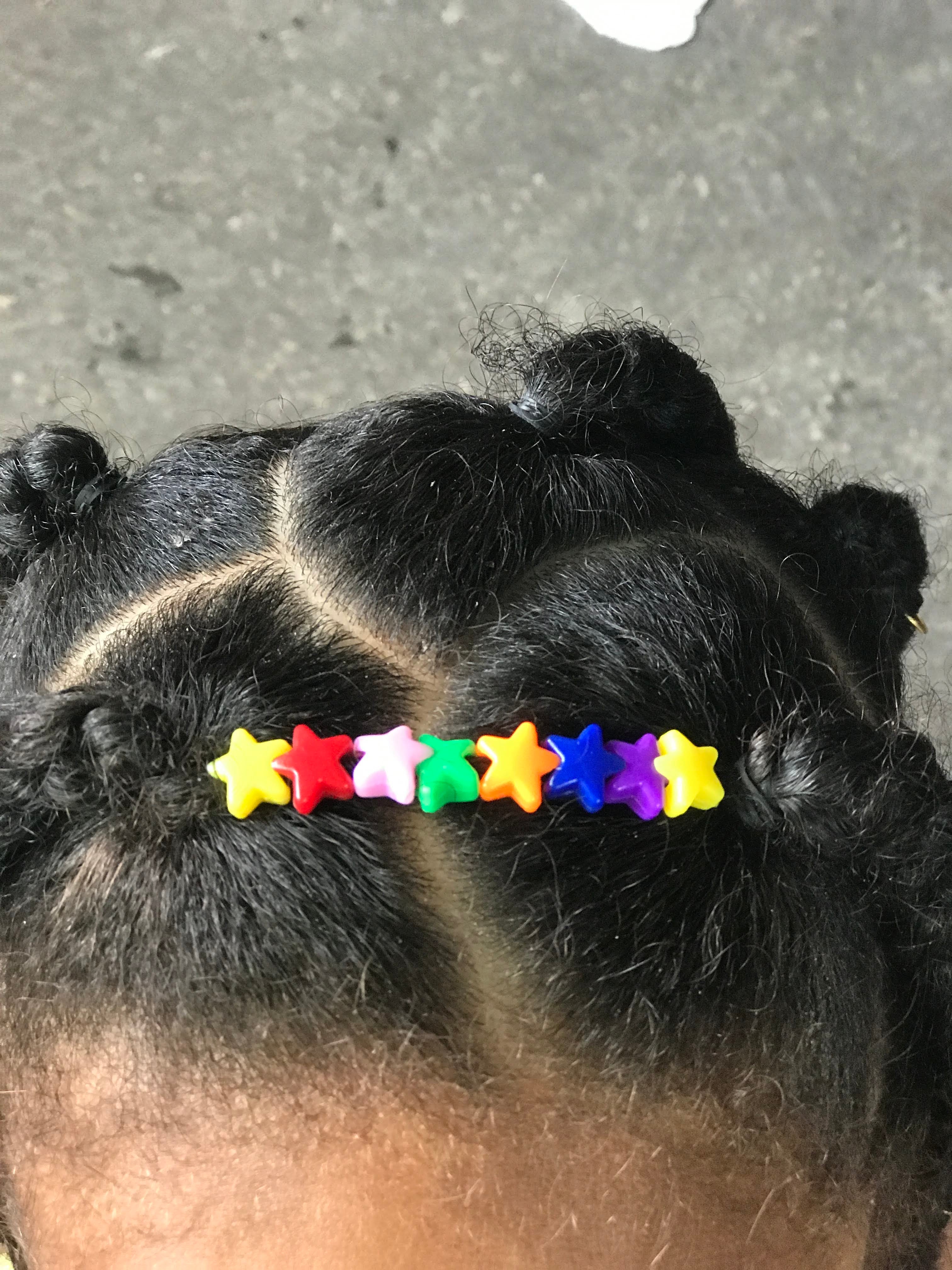 Gros plan sur les perles étoiles multicolores ornant la racine d'une coiffure twist pour enfant.